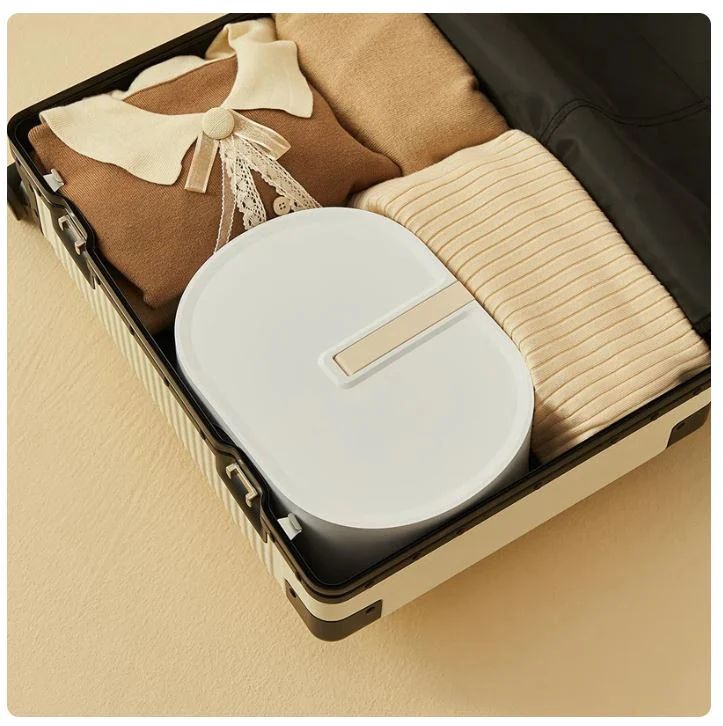 Compact electric clothes drying machine packed in suitcase with folded sweaters for travel convenience